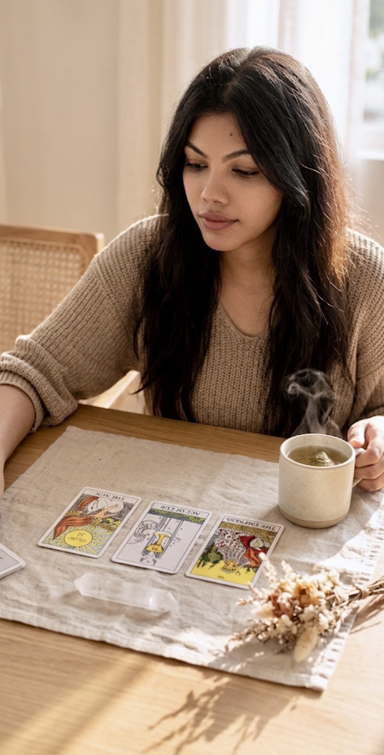 Woman reading tarot cards at a table with tea and dried flowers — signs you need a tarot reading